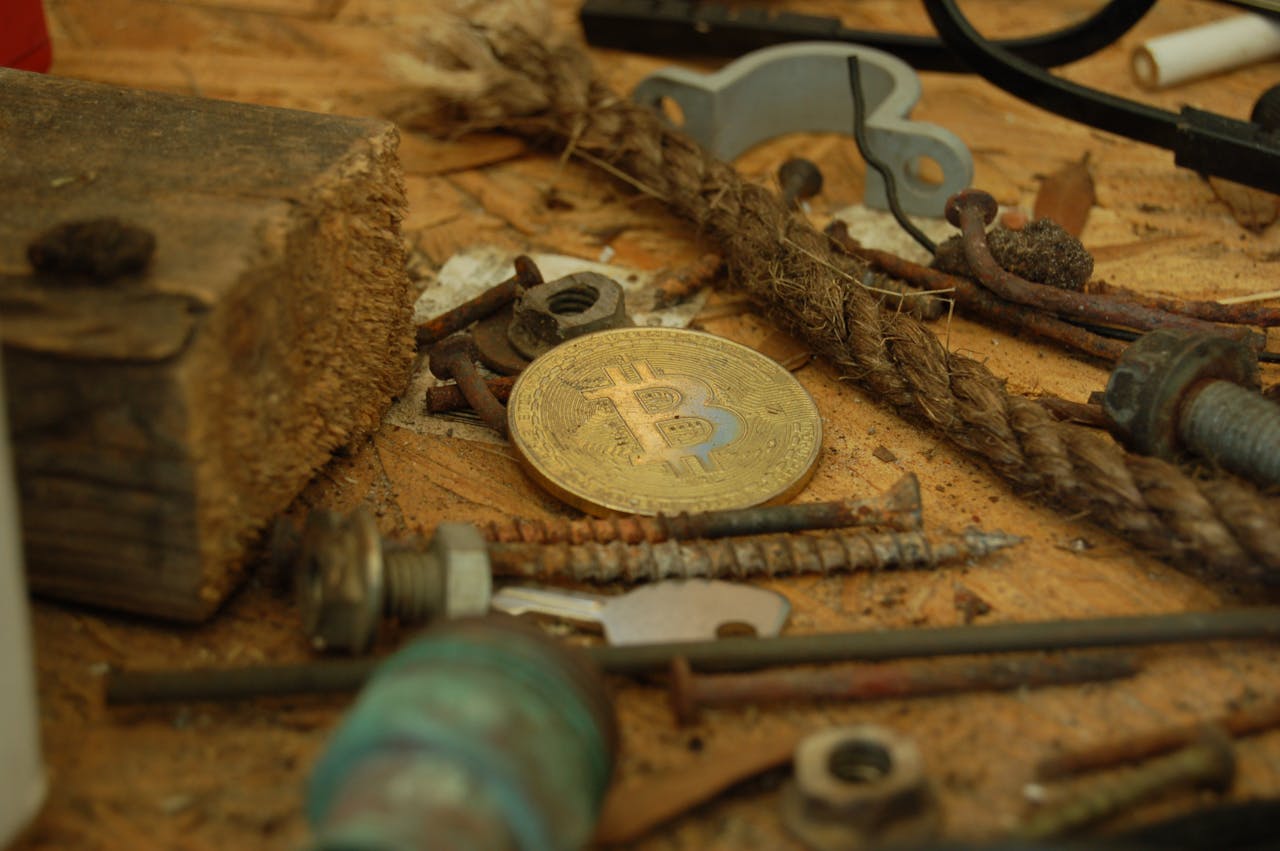 A bitcoin coin placed among various tools and hardware pieces on a wooden surface.