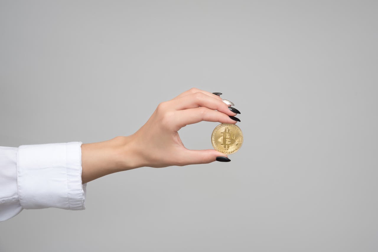 Close-up of a womans hand holding a bitcoin coin against a neutral background.